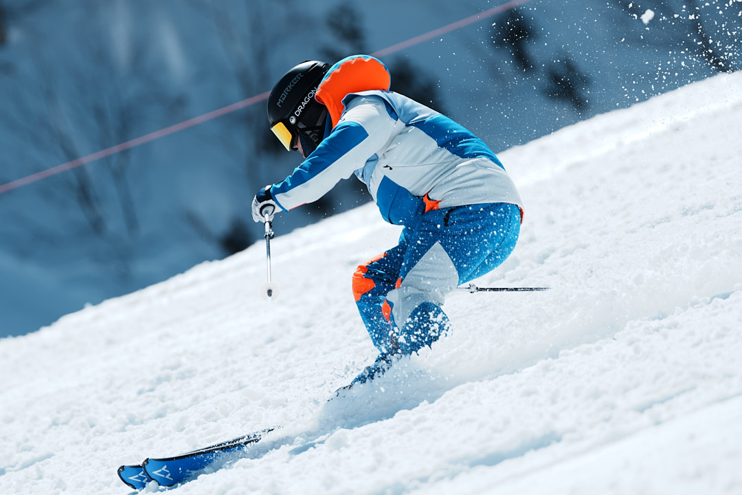 雪を巻き上げてターンする、白いゼッケンの選手