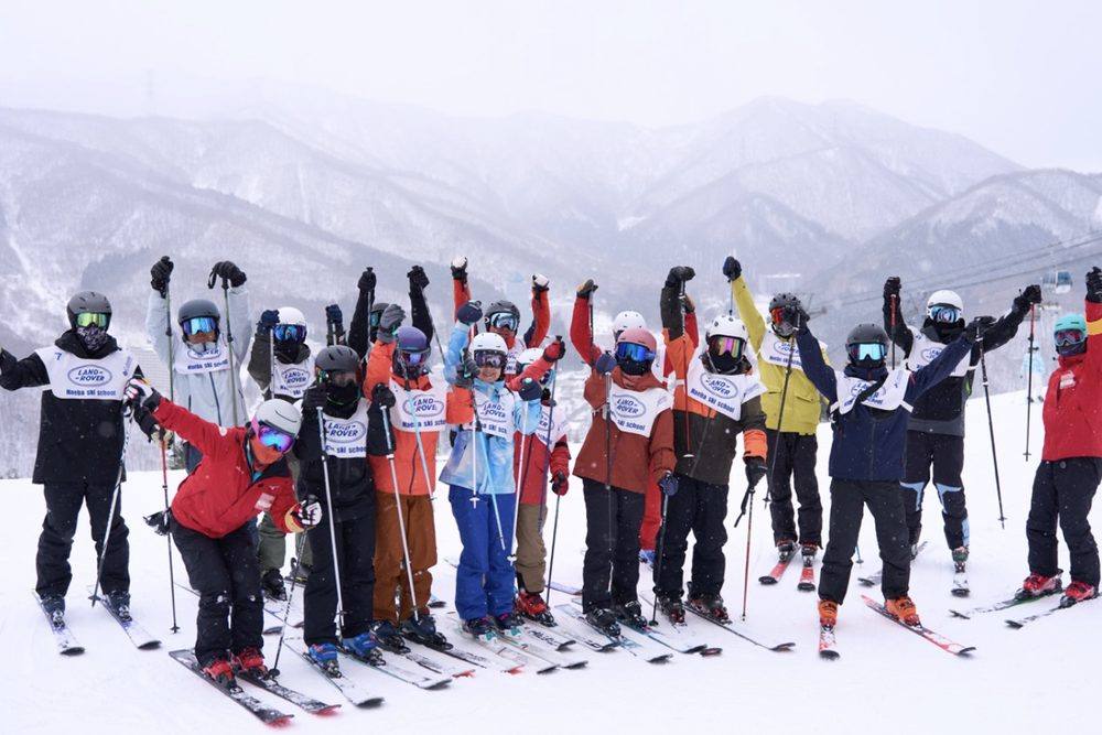 雪山を背に、ストックを掲げて喜ぶ検定キャンプの受講生とコーチ